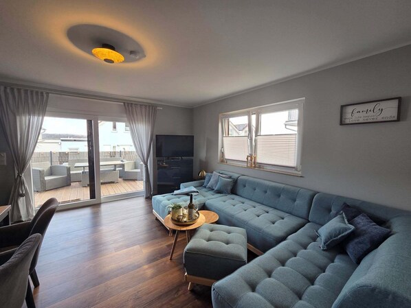 A modern living room with a sofa, a TV, and a view of the outside.