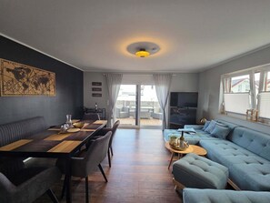 Ein modernes Wohnzimmer mit Essbereich, einer Couch, einem Fernseher und Blick ins Freie.