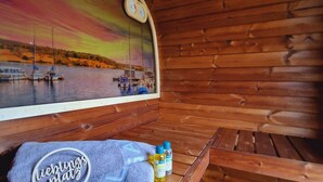A wooden cabin with a mural of a sunset over a lake, a towel with "Liebingplatz" text, and toiletries on a bench.