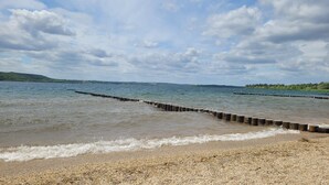 A pebbled beach with a wooden breakwater extending into a calm lake.