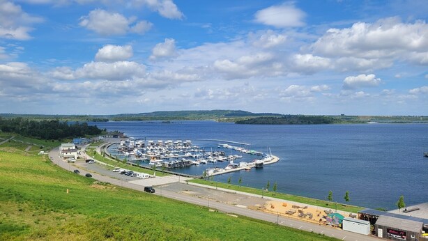 A marina with boats docked, a road leading to the marina, and a small building with a sign.