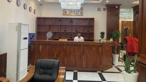 A hotel reception area with a wooden reception desk, a black leather chair, a chandelier, and a checkered floor. - Phat Power Hotel (Sihanoukville)