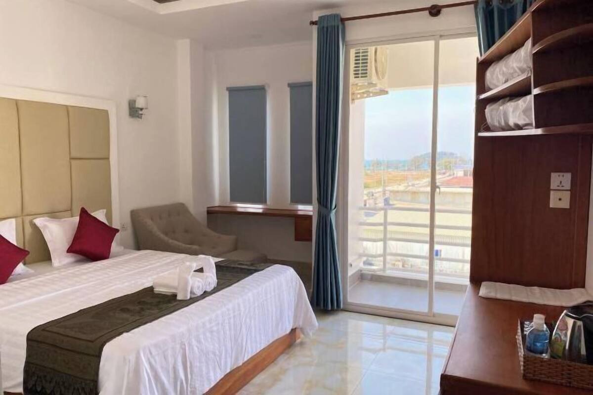 A hotel room with a bed, a chair, a desk, and a view of the outside.
