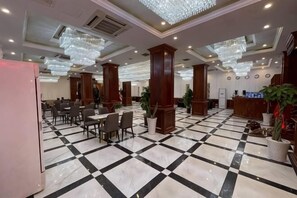 Eine Hotelhalle mit Schachbrettfußboden, Kronleuchtern, Holzsäulen und einer Rezeption.