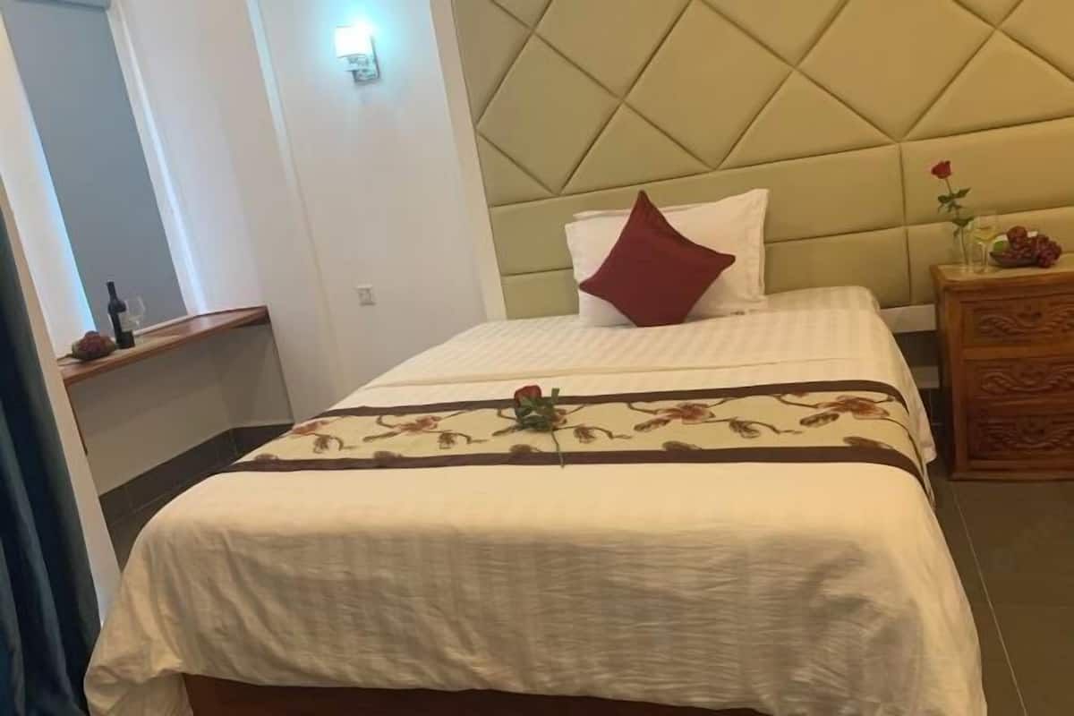 A hotel room with a bed, a nightstand, and a wooden dresser.