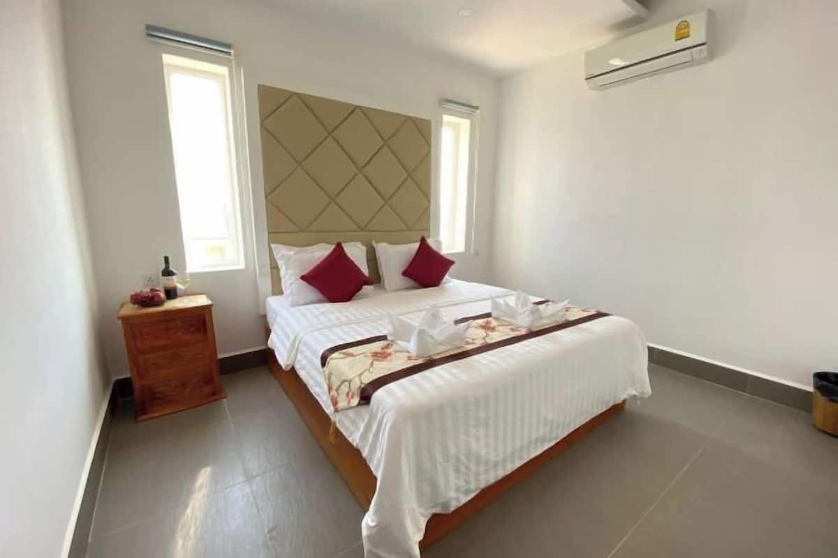 A bedroom with a bed, a wooden nightstand, a window, and an air conditioning unit.