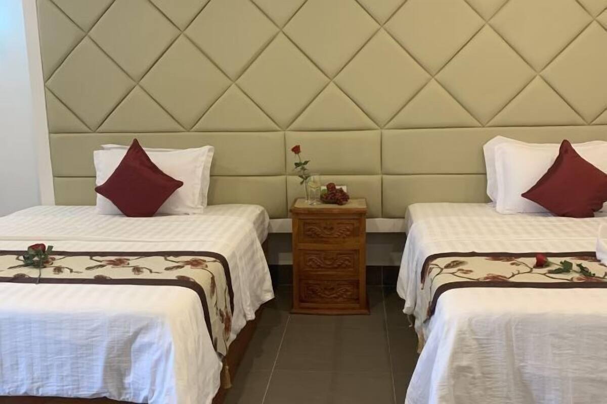 A hotel room with two beds, a padded headboard, a wooden nightstand, and a floral bedspread.