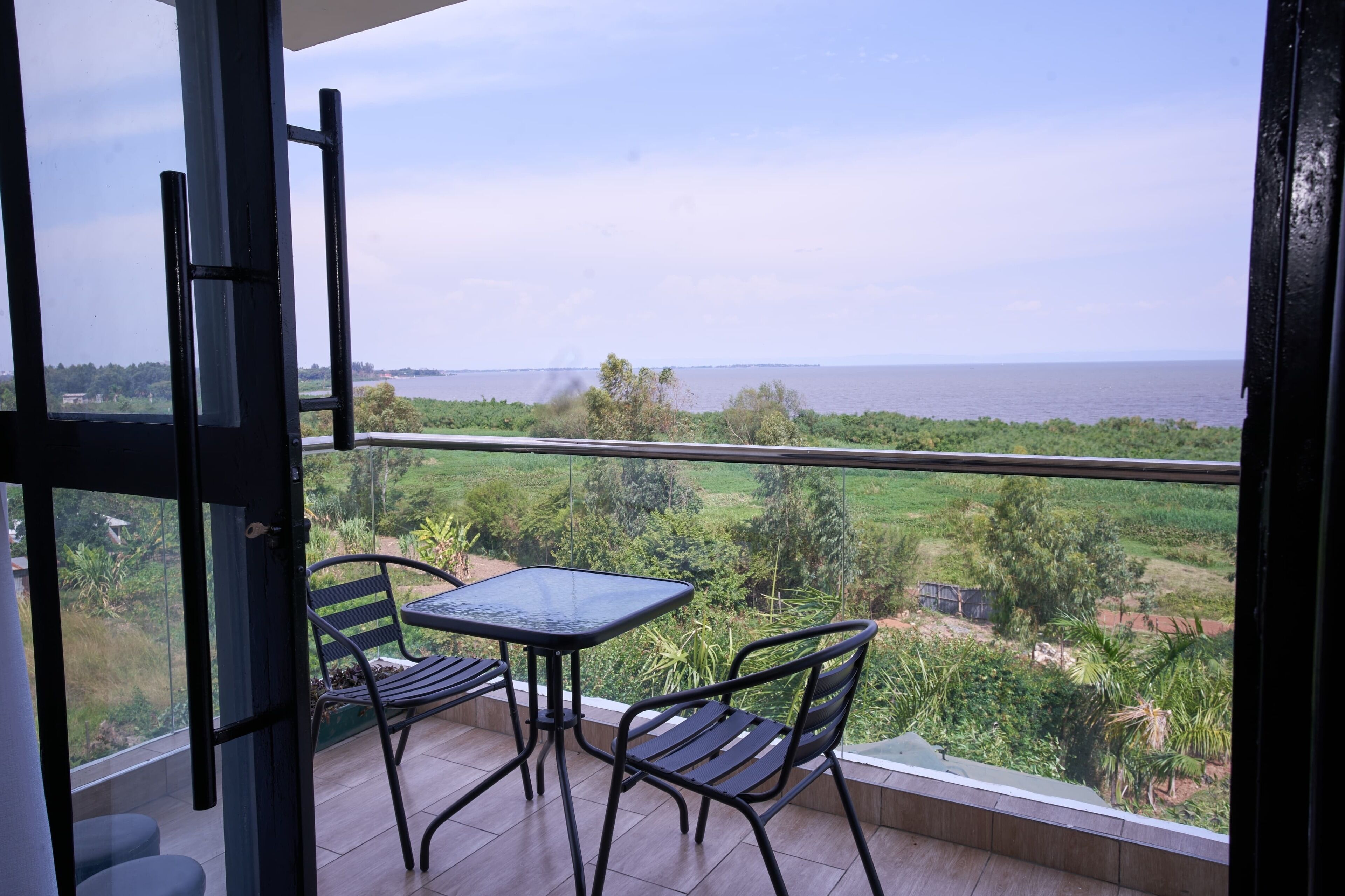 Een balkon met een tafel en stoelen, met uitzicht op water en groen.
