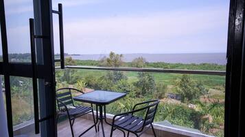 Een balkon met een tafel en stoelen, met uitzicht op water en groen.
