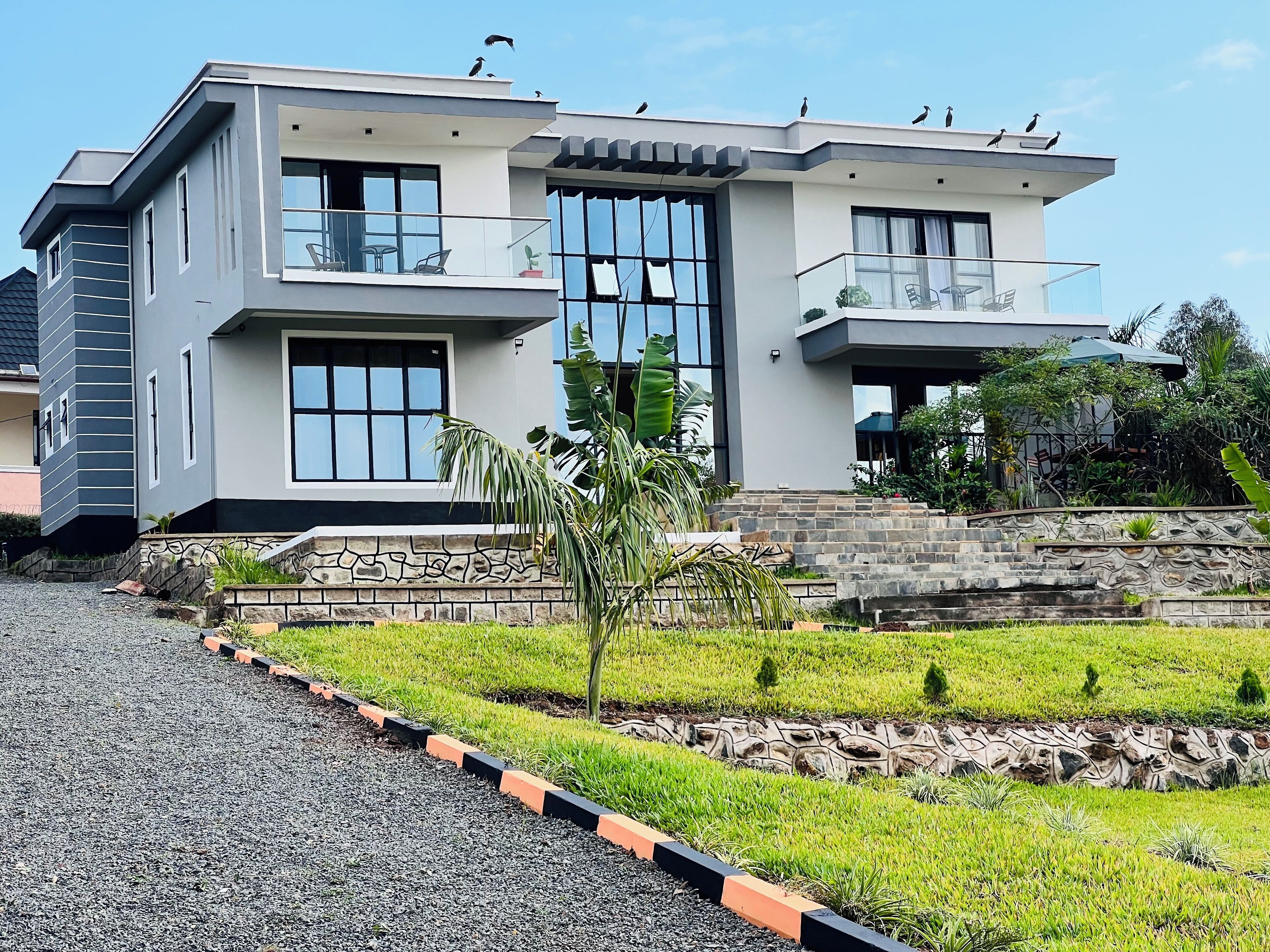 A modern two-story house with a balcony, large windows, and a stone staircase leading to the entrance.