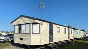 A mobile home with a satellite dish, a small porch, and a garage. - GC132 - Discover Your Perfect Seaside Escape in Clacton-on-Sea! (Saint Osyth)