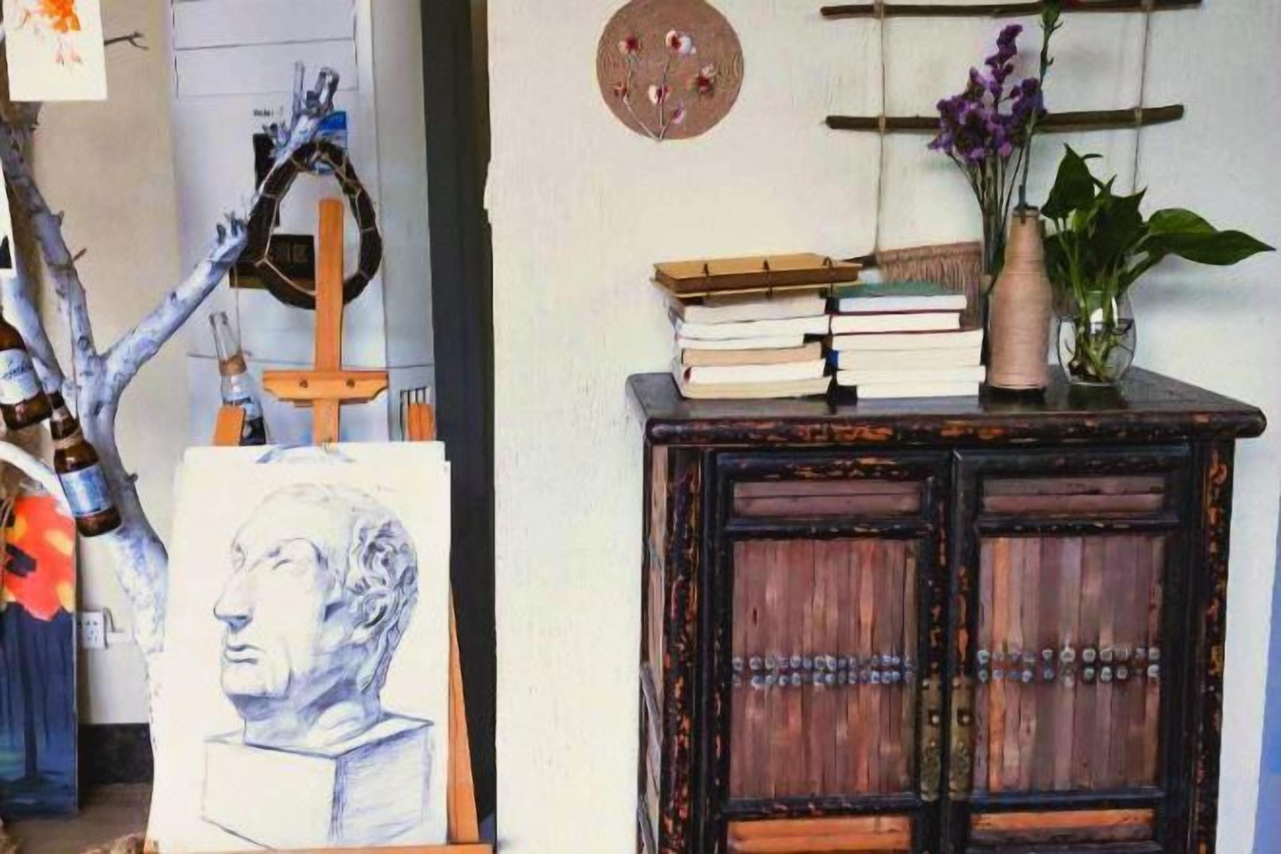 A room with a wooden cabinet, a vase with flowers, and a painting on the wall.