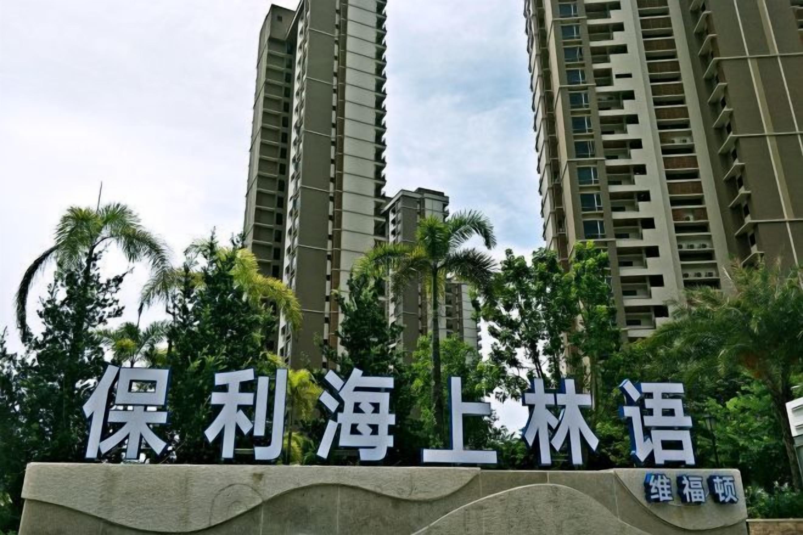 A sign with Chinese characters, indicating a residential area with tall buildings and palm trees in the background.