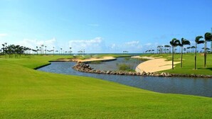 A golf course with a water hazard, sand bunkers, and palm trees. - Weifudun Holiday Apartment (Hailing Island Poly Silver Beach) (Yangjiang)