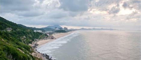 A coastal landscape with a beach, rocky shoreline, and a hilly backdrop.