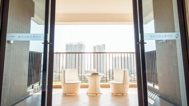 A balcony with two white chairs and a small table, overlooking a cityscape with high-rise buildings. - Weifudun Holiday Apartment (Hailing Island Poly Silver Beach) (Yangjiang)