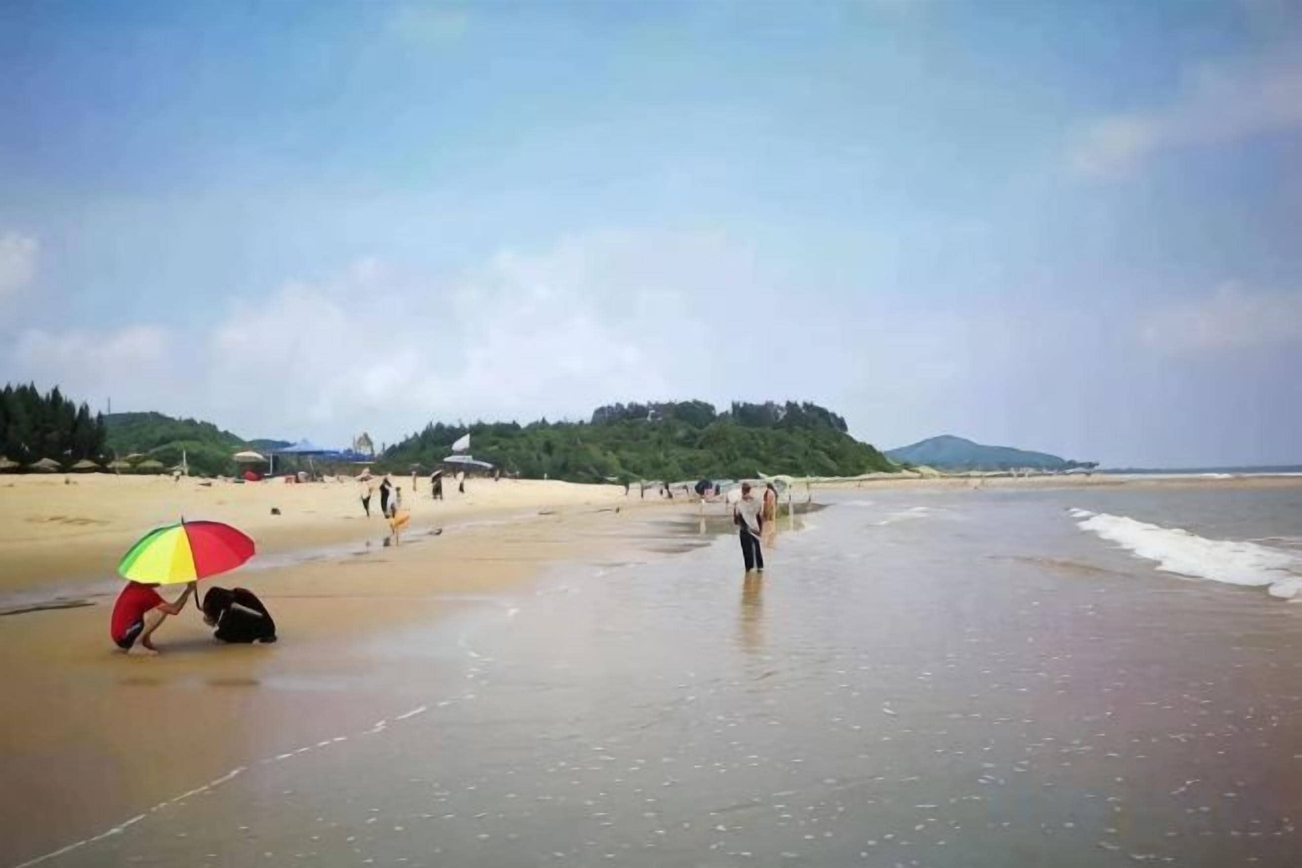 A beach with people, a colorful umbrella, and a clear sky.