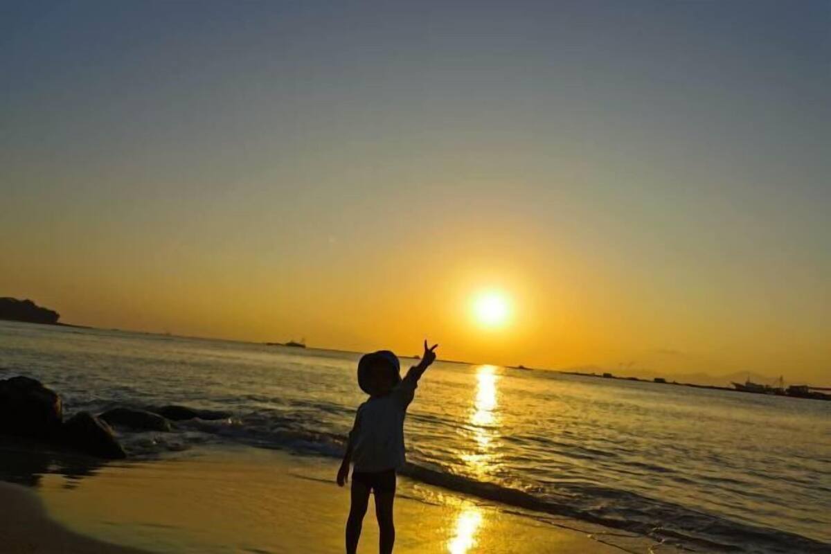 Un niño de pie en la playa mirando la puesta de sol.