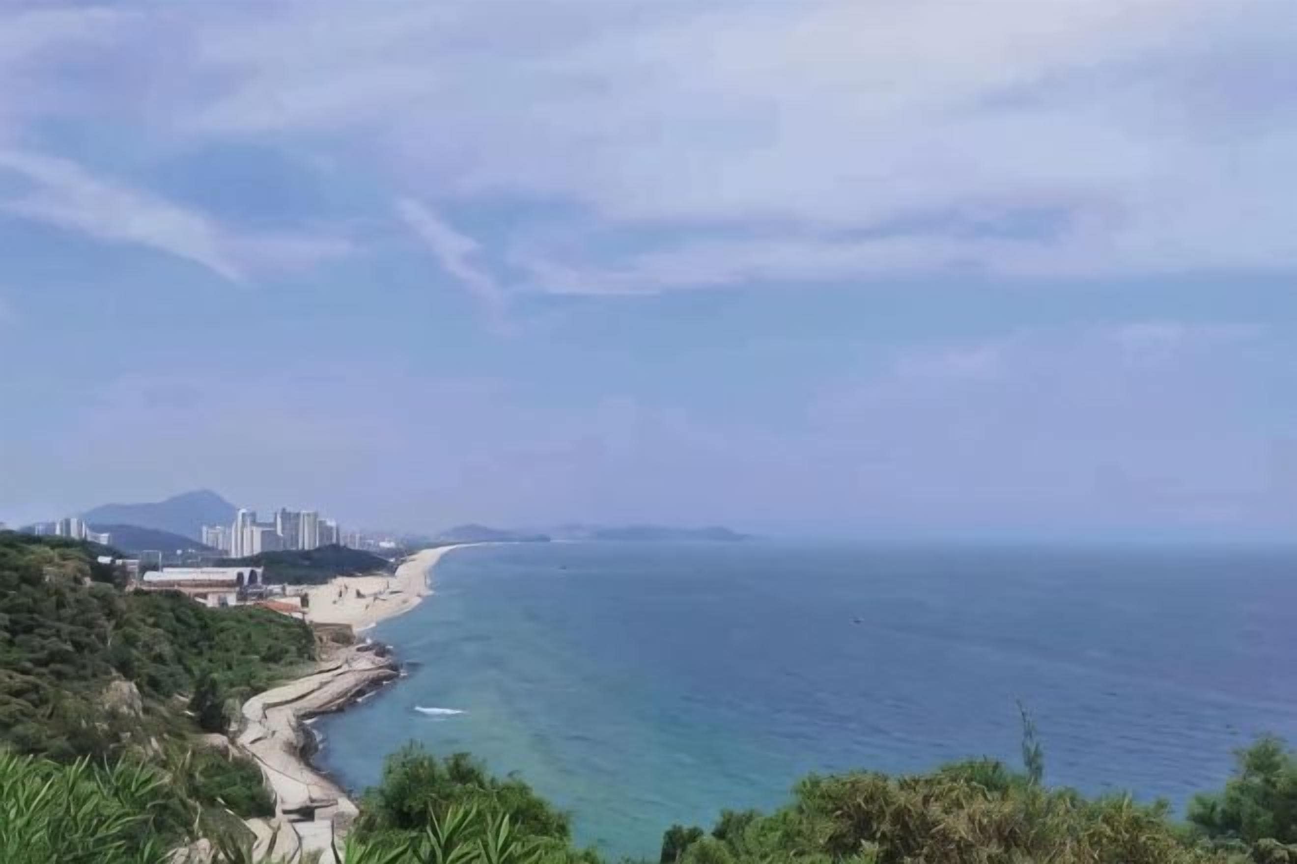 Un paisaje costero con una playa, un camino sinuoso y edificios a lo lejos.