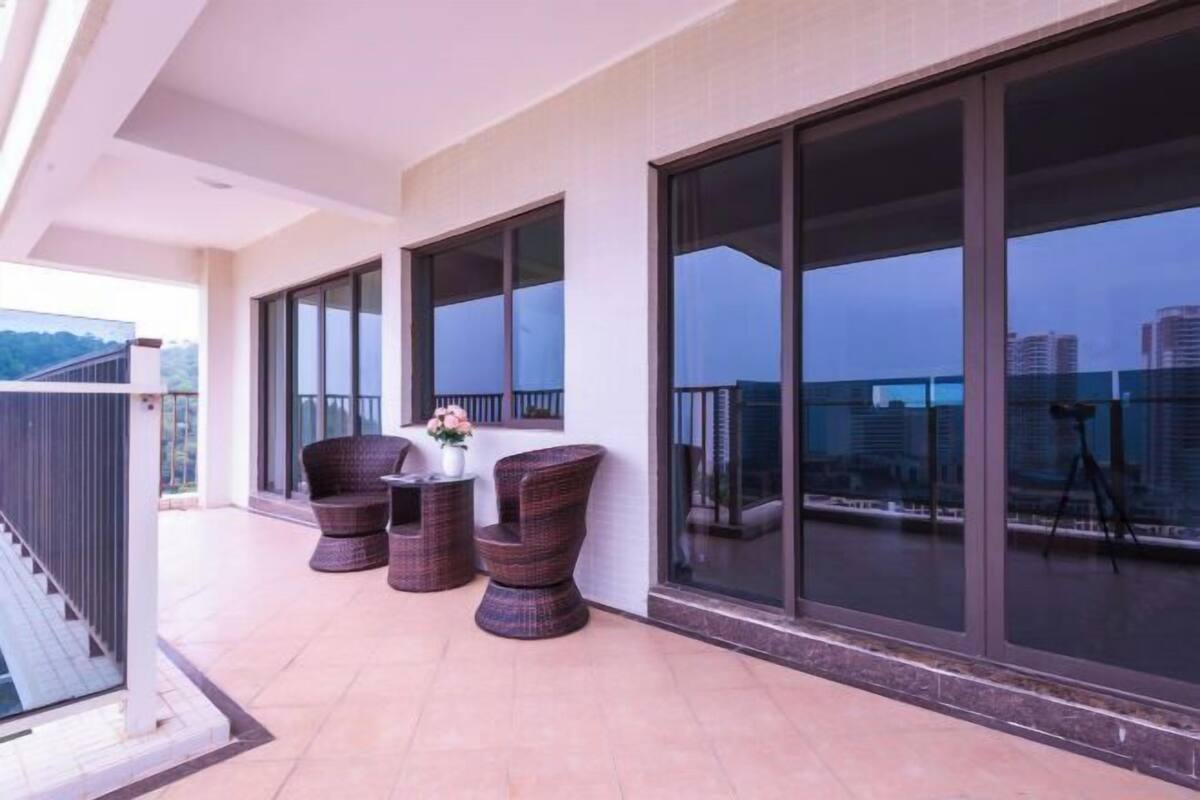 Un balcón con mobiliario de mimbre y ventanas amplias que dan a un paisaje urbano.