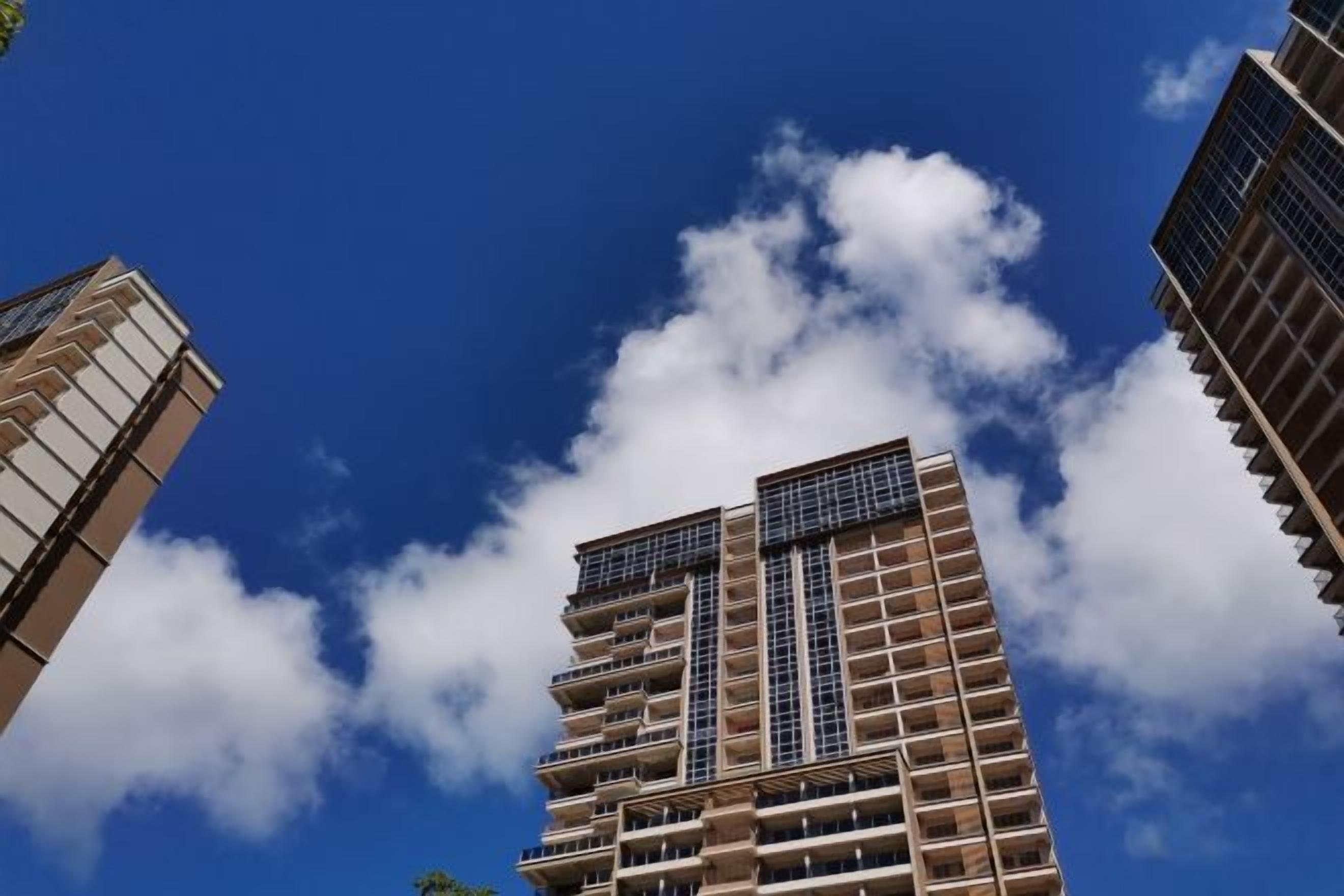 A high-rise building with multiple floors and balconies, under a clear blue sky with clouds.