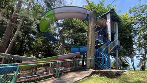 Um parquinho com escorrega e escadas, cercado por árvores e um edifício.