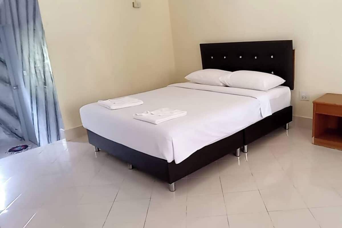 Una cama bien hecha con sábanas y almohadas blancas, una mesita de noche de madera y un piso de baldosas.