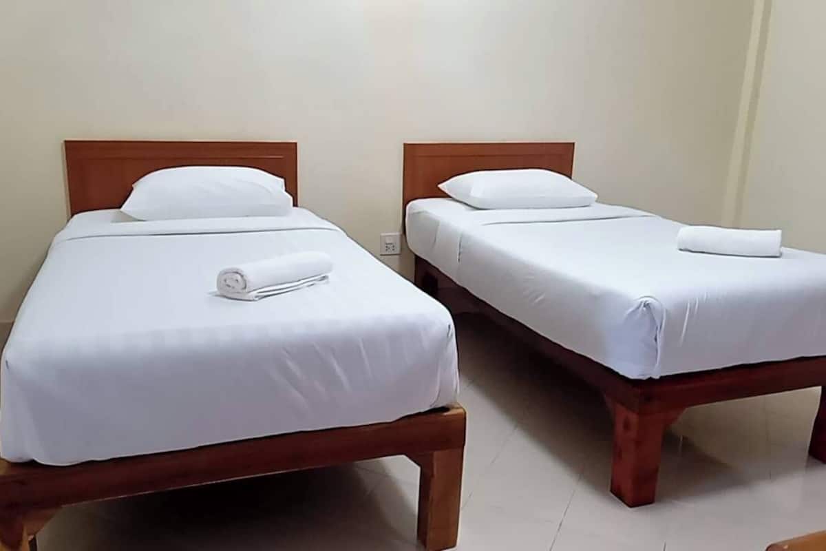 Dos camas individuales con cabeceros de madera y ropa blanca, cada una con una almohada y una toalla enrollada.
