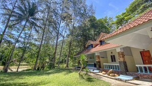Uma casa com telhado de telhas, escadaria de pedra e um gramado com árvores.