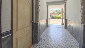 Um corredor com piso de azulejos, porta de madeira e vista para o exterior.