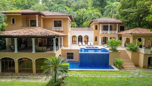 Ein großes, mehrstöckiges Haus mit Swimmingpool, Sitzgelegenheiten im Freien und üppiger Bepflanzung.