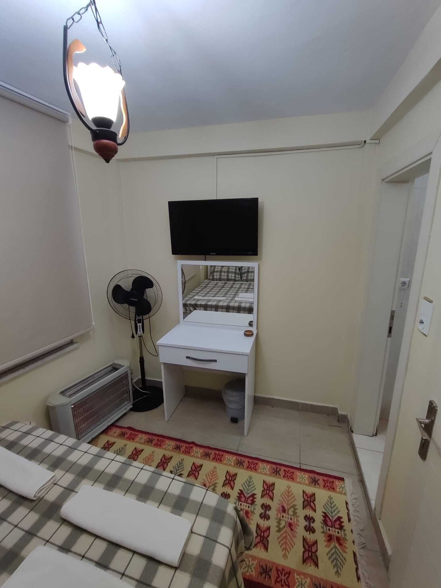 A bedroom with a bed, a desk, a chair, a standing fan, and a heater.