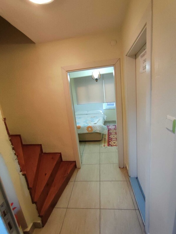 Un estrecho pasillo que conduce a un dormitorio con cama, mesita de noche y ventana.