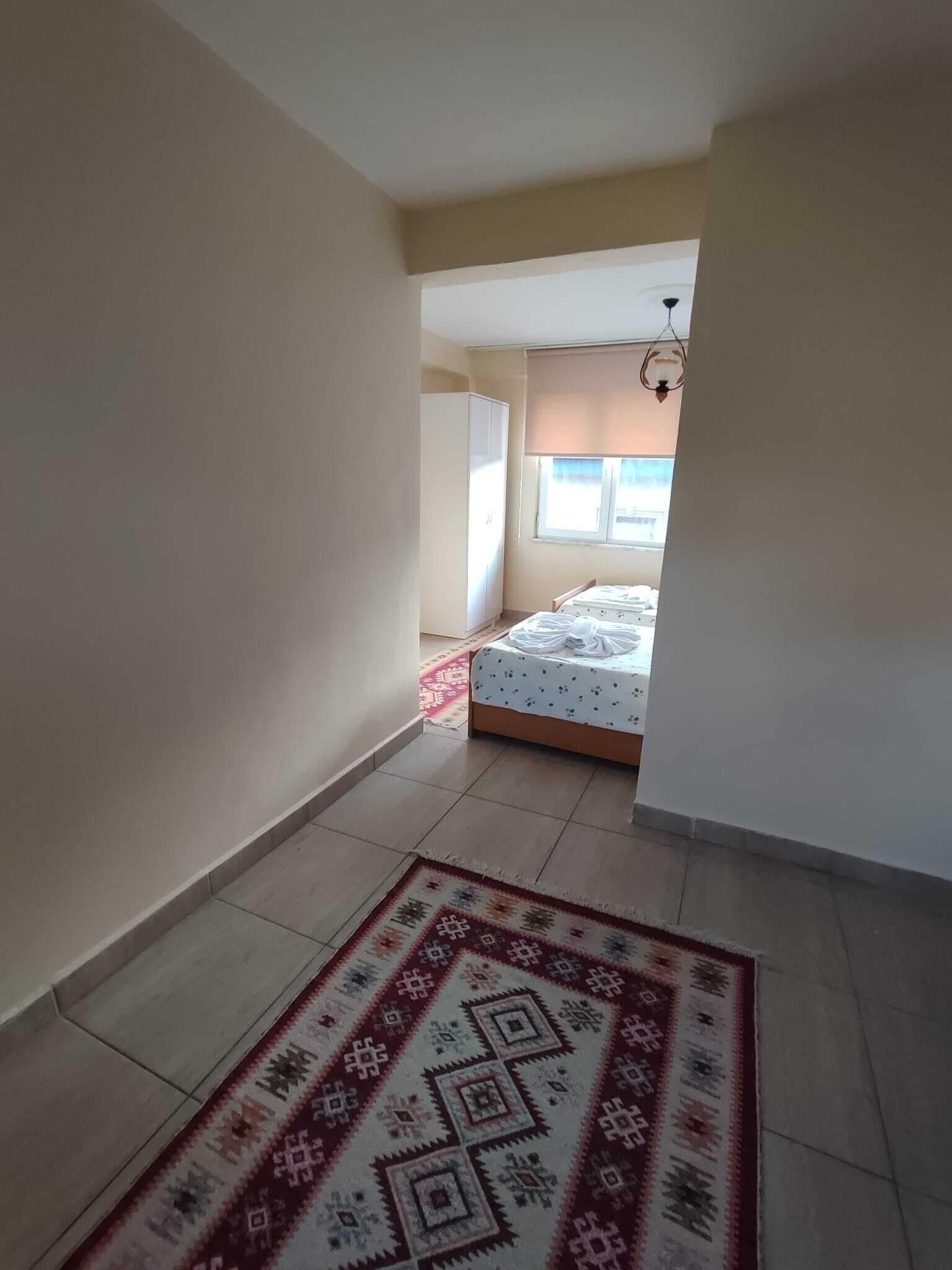 Un estrecho pasillo con un tapete estampado que lleva a un dormitorio con cama y ventana.