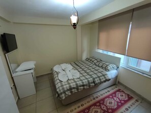 Una habitación pequeña y limpia con una cama, una mesita de noche, un espejo y una ventana con persianas.