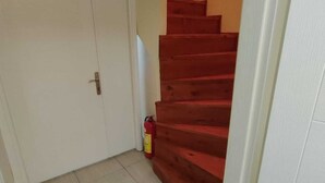 A hallway with a closed door, a tiled floor, and a wooden staircase. - Çarşı Marin Denizer Pension (Amasra)