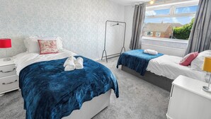 A bedroom with two beds, a window with curtains, a radiator, and a bedside table with a lamp.