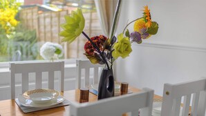 A dining table with white chairs, a vase with flowers, and a plate with a bowl.