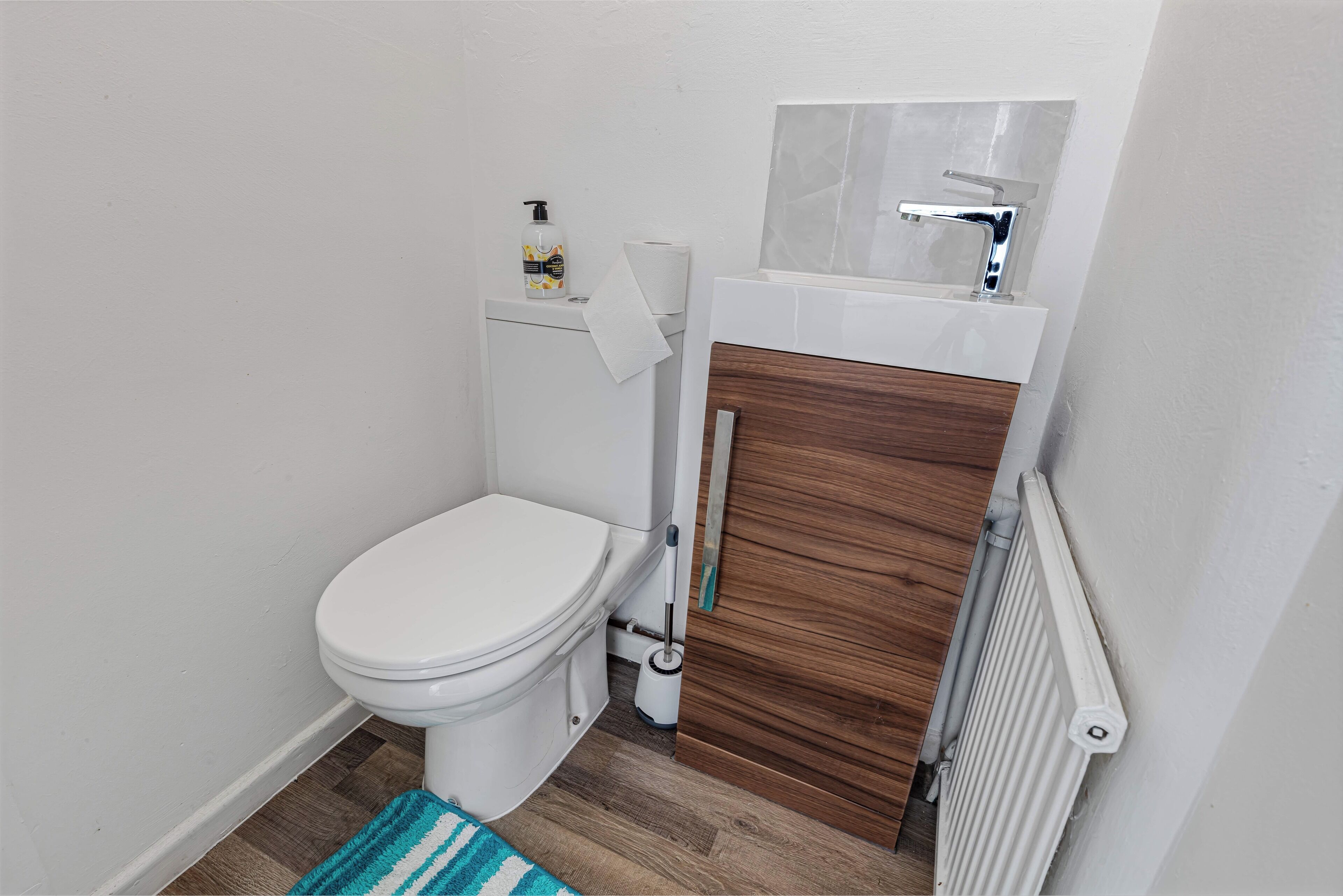 Une petite salle de bain avec des toilettes blanches, un meuble-lavabo en bois, un lavabo blanc et un radiateur.