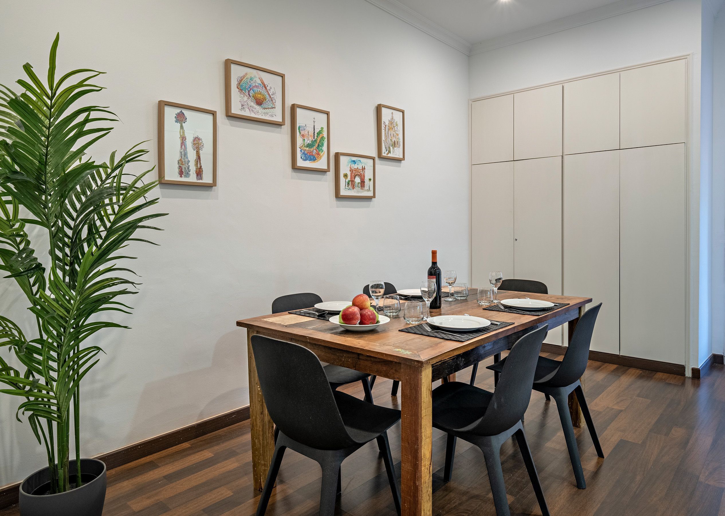 Un comedor con mesa de madera, sillas negras y cuadros en la pared.