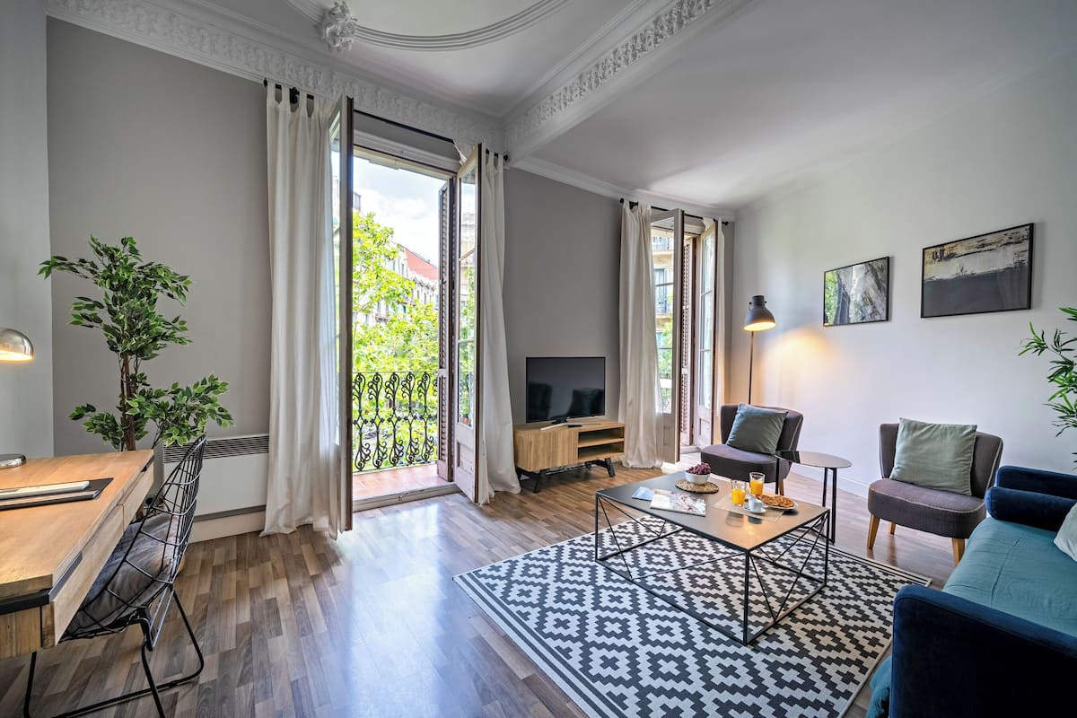 A modern living room with a wooden dining table, a sofa, a TV, and a balcony with curtains.