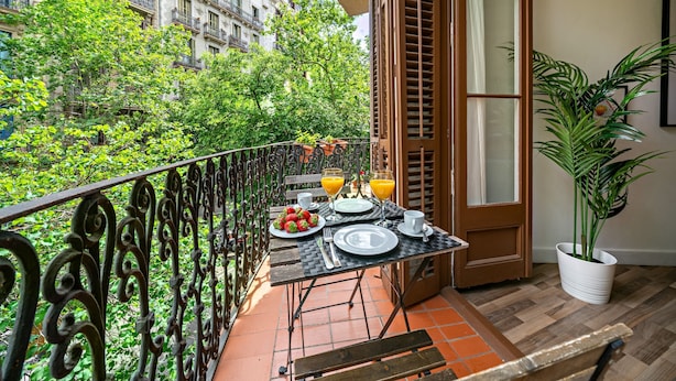 A balcony with a table set for breakfast, surrounded by greenery and buildings. - Habitat Apartments Barcelona Balconies (Barcelona)
