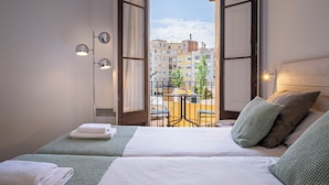 A hotel room with two beds, a balcony with a table and chairs, and a view of buildings. - Habitat Apartments Barcelona Balconies (Barcelona)