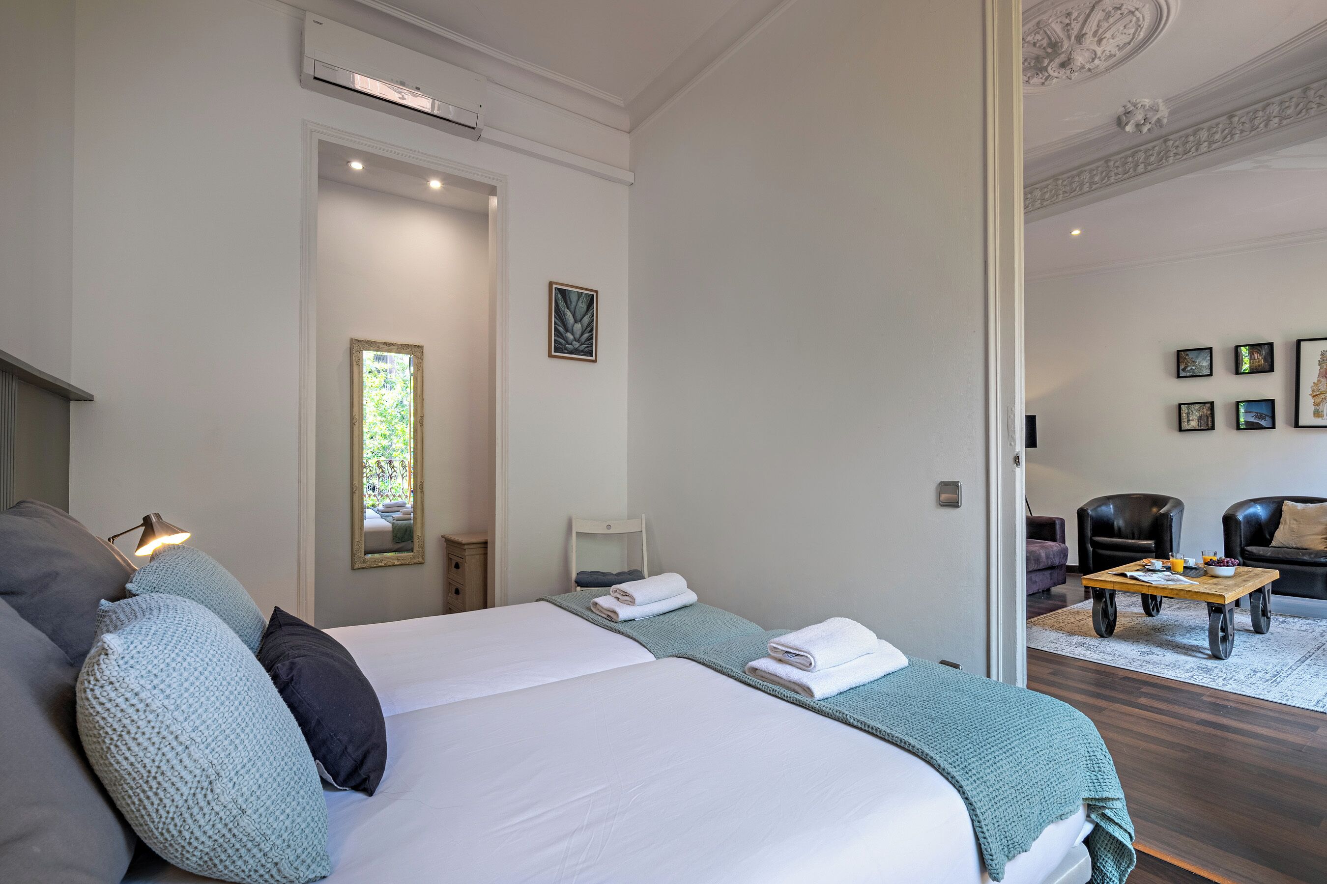 Quarto de hotel moderno com uma cama grande, um espaço de estar com mesa de centro e vista através de uma porta aberta.
