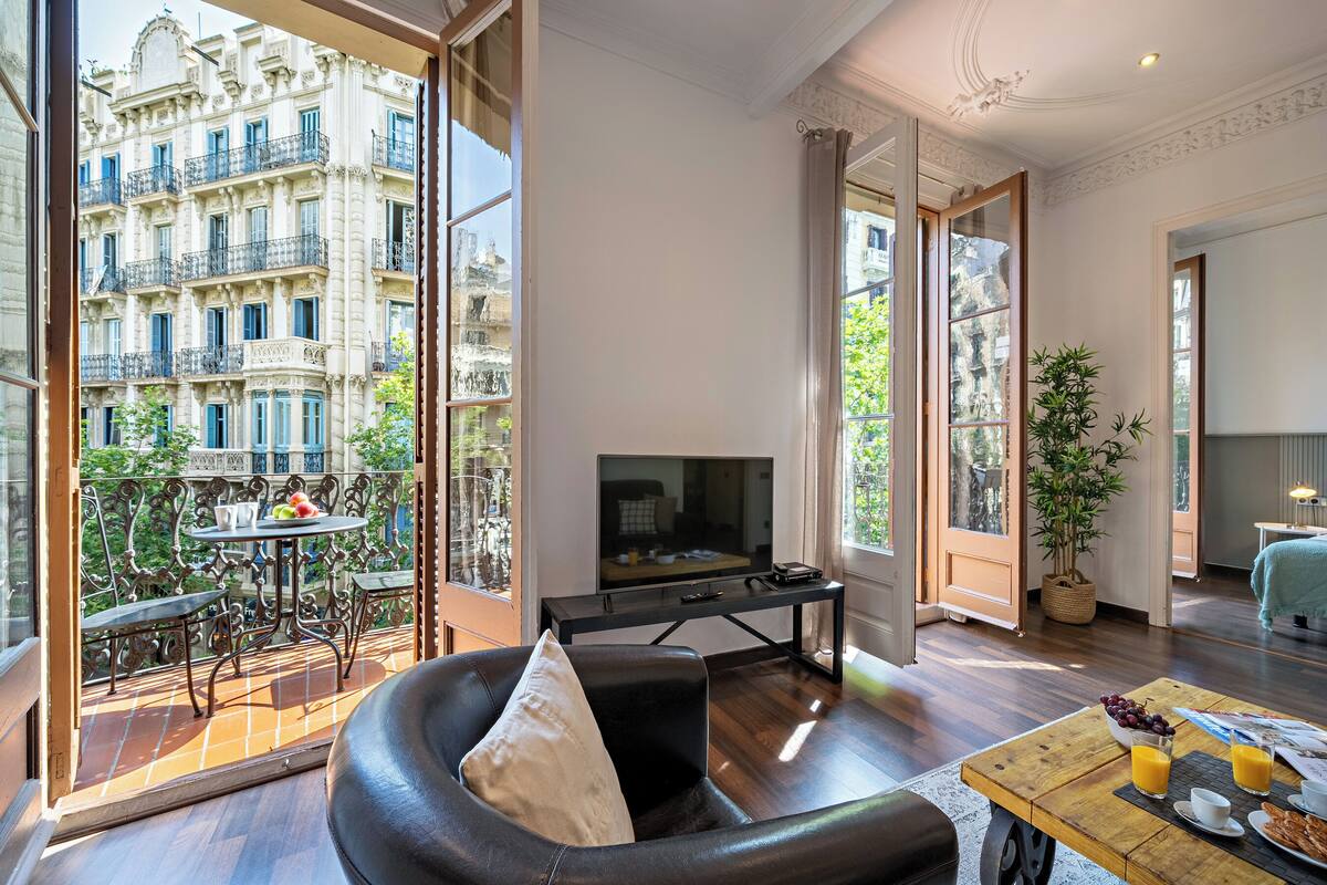 A modern living room with a large TV, wooden furniture, and a balcony with a view of a historic building.