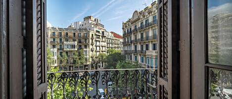 A balcony with wrought iron railings overlooking a street with buildings and cars.