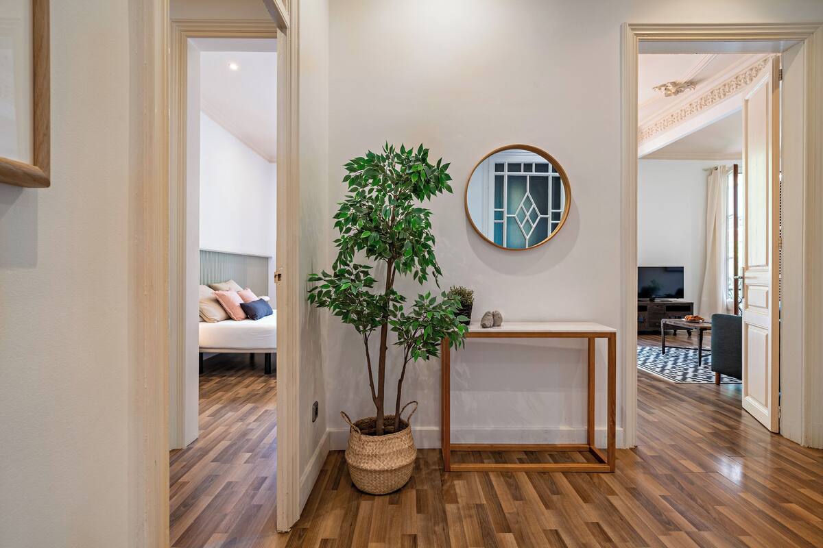 A hallway with wooden flooring, a potted plant, a round mirror, and a white console table.
