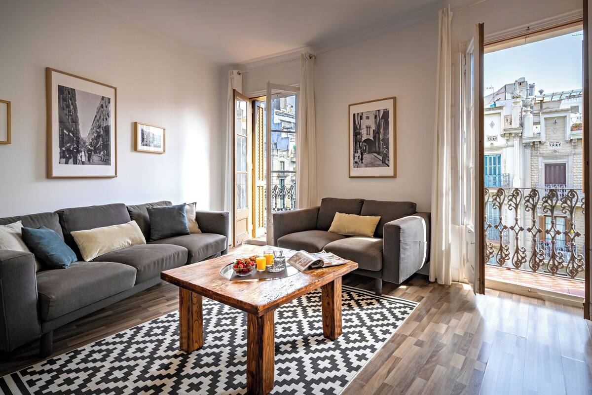 A modern living room with a sofa, a coffee table, and a balcony with a wrought iron railing.
