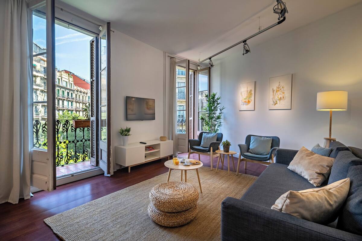 A modern living room with a grey sofa, a round coffee table, and a large window with a view of buildings.