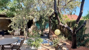 An outdoor patio with a wooden table and chairs, surrounded by stone walls and greenery. - La villa au palmier - 10bed, 2bath, roof terrace (Perpignan)